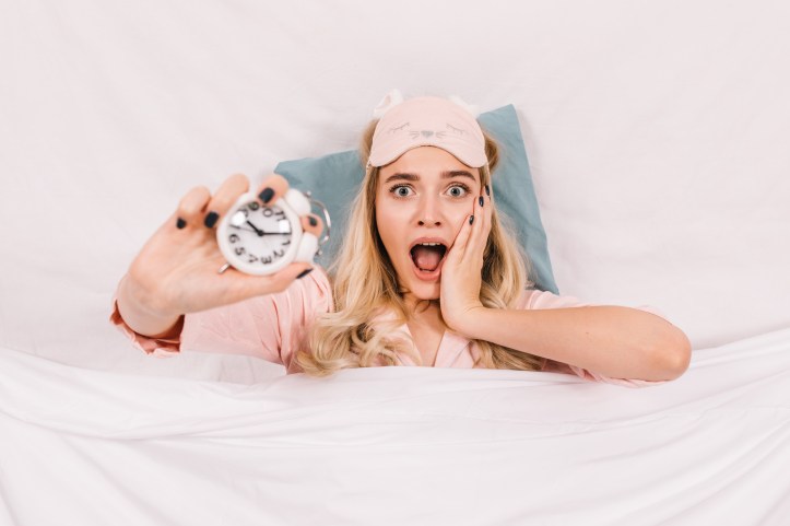 Femme surprise tenant un réveil dans son lit, illustration humoristique d’une inquiétude exagérée sur la durée de sommeil.